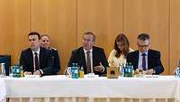 Schmid, Pistorius und Kiesewetter sitzen an einem Tisch während einer Veranstaltung.