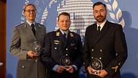 eine Soldatin und zwei Soldaten posieren mit einem runden gläsernen Preis