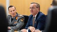 Minister Pistorius im dunkelblauen Anzug neben einem Soldaten im Dienstanzug