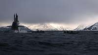 Ein aufgetauchtes U-Boot setzt Soldaten ab. Im Hintergrund sind schneebedeckte Berge zu sehen.