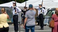 drei Soldaten in blau-weißer Uniform in strammer Haltung präsentieren Gewehre in einer Vorführung vor Publikum