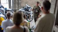 ein Soldat erklärt vor Gruppe im Treppenhaus des Ministeriums vor großen Motorrädern die Aufgaben der Feldjäger