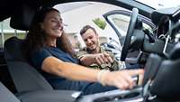 eine lockige Frau in einem Auto bekommt von einem Soldaten die Technik des Fahrzeuges gezeigt