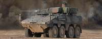 Ein Radpanzer steht im Gelände. Im Hintergrund ist eine Staubwolke zu sehen.