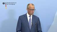 Friedrich Merz steht an einem Rednerpult vor einer blauen Wand und spricht.