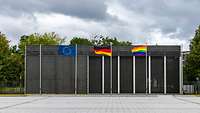 Eine Regenboggenflagge ist neben der EU- und Deutschlandflagge gehisst und weht im Wind.