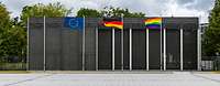 Eine Regenboggenflagge ist neben der EU- und Deutschlandflagge gehisst und weht im Wind.