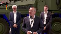 Boris Pistorius steht an einem Mikrofon und spricht. Im Hintergrund ist ein Radpanzer zu sehen.