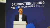 Nils Schmid steht an einem Rednerpult und spricht. Im Hintergrund ist eine blaue Wand mit einem Logo.
