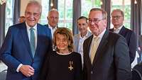 Bayerns Innenminister und der Verteidigungsminister stehen zusammen mit einer Ehrenkreuzempfängerin