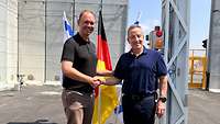 zwei Männer vor einer grauen Betonmauer geben sich die Hand
