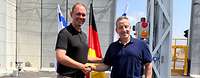 zwei Männer vor einer grauen Betonmauer geben sich die Hand