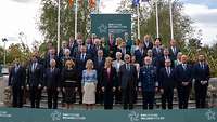 Mehrere Personen stehen für ein Gruppenfoto zusammen. Die Flaggen von Irland und Europa wehen an Masten.