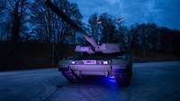Der Kampfpanzer Leopard 2 A8 steht auf einem Gelände bei Dunkelheit. 