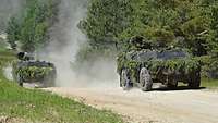 Zwei mit Grünzeug getarnte Militärfahrzeuge fahren über Sandboden