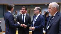 Staatssekretär Hartmann steht mit 4 weiteren Männern im Halbkreis und spricht mit ihnen.