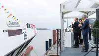 Mehrere Personen stehen klatschend vor einem Schiff.