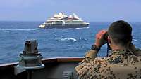 Soldat mit Fernglas von der Brücke eines Militärschiff ein Kreuzfahrschiff auf See