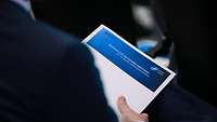 Jemand hält ein Dokument mit dem Titel NATO´s CUI-Network Meeting in der Hand