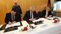 Schneider, Hoofe und eine weitere Person unterzeichnen eine Vereinbarung