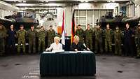 Von der Leyen und Amtkollegin Hennis-Plaschaert sitzen an einem Tisch vor angetretenen Soldaten.
