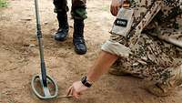 Ein deutscher Soldat erklärt einem malischen Soldaten die Verwendung von Metalldetektoren