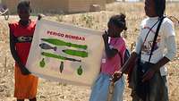 Afrikanische Mädchen halten ein Plakat mit darauf abgebildeten Minen