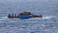 Menschen werden von Soldaten mit Speedbooten aus einem überfüllten Boot gerettet.